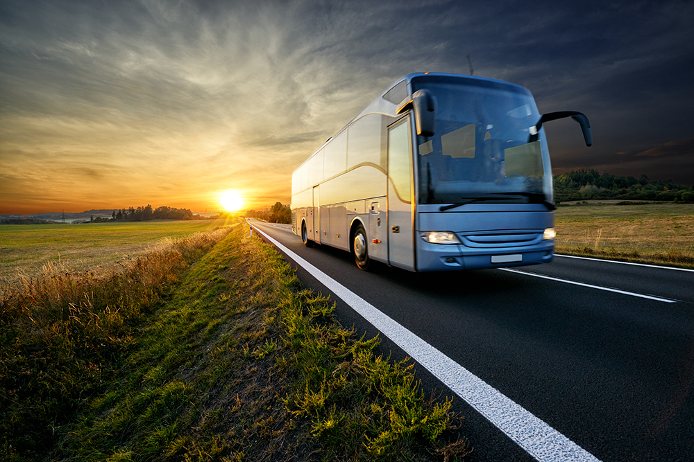 Bus auf der Asphaltstraße in der ländlichen Landschaft bei Sonnenuntergang fahren